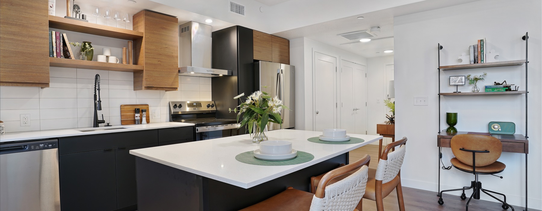 An interior view of a kitchen island countertop with stainless steel appliances, and views of a hallway with closet doors in a one bedroom apartment at The Source on South Temple in Salt Lake City, Utah.